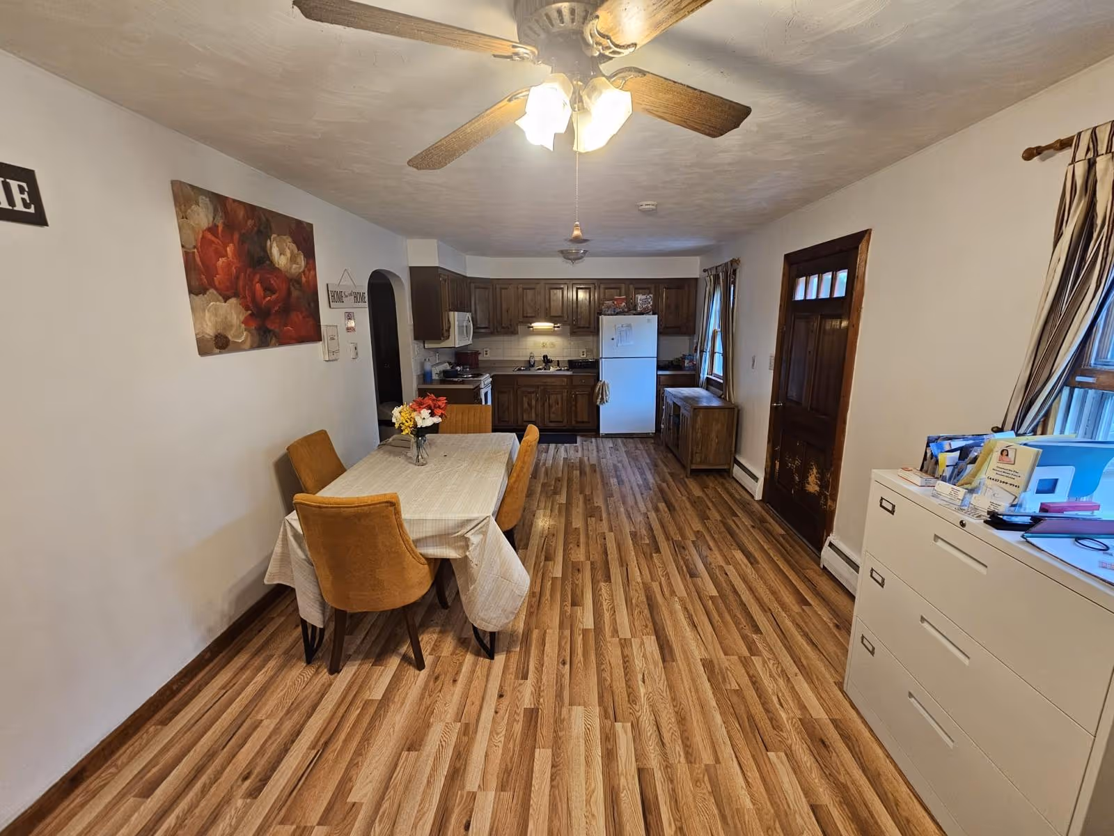 Dining area with table and four tan chairs, kitchen cabinets, and a ceiling fan overhead.