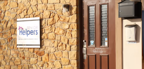 Stone exterior wall with a Senior Helpers sign and brown front door.