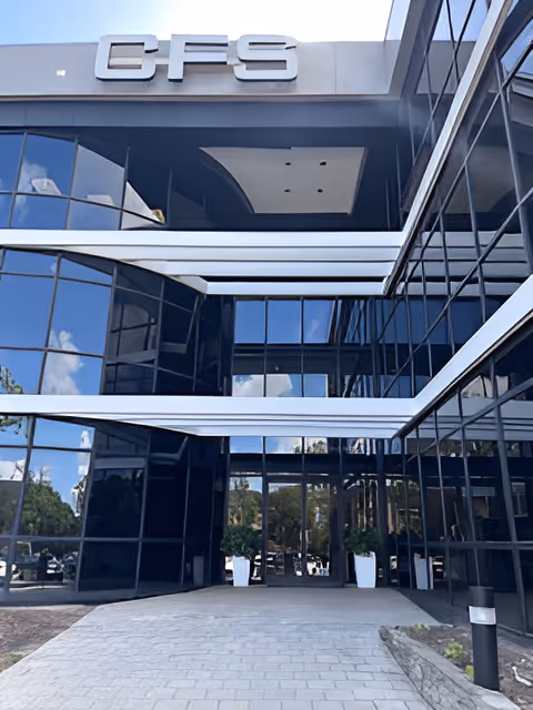 Modern glass-fronted building entrance with a covered walkway and reflective blue-tinted windows.