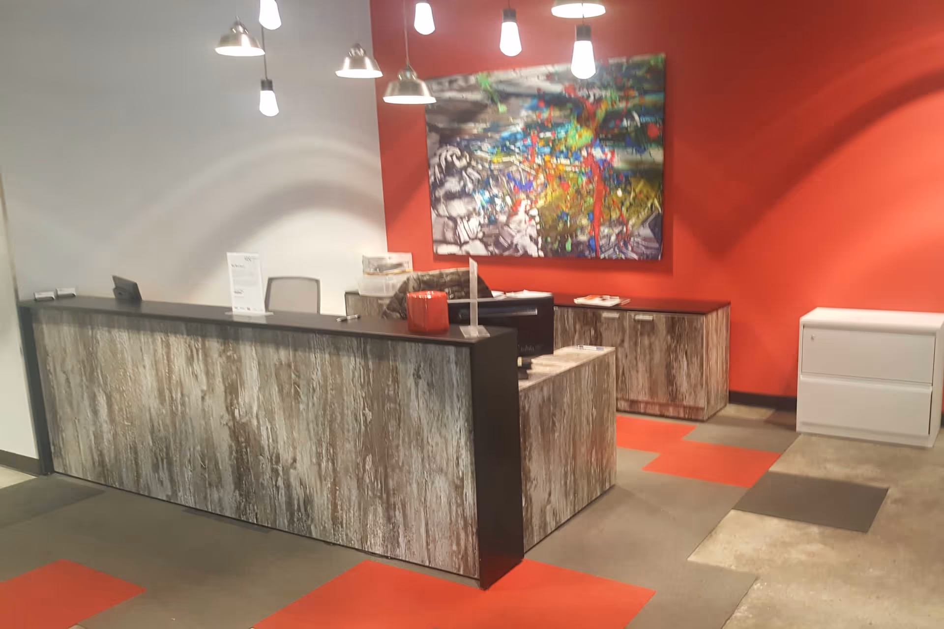 Reception area with wood-front desk, red wall, pendant lights, and colorful artwork.