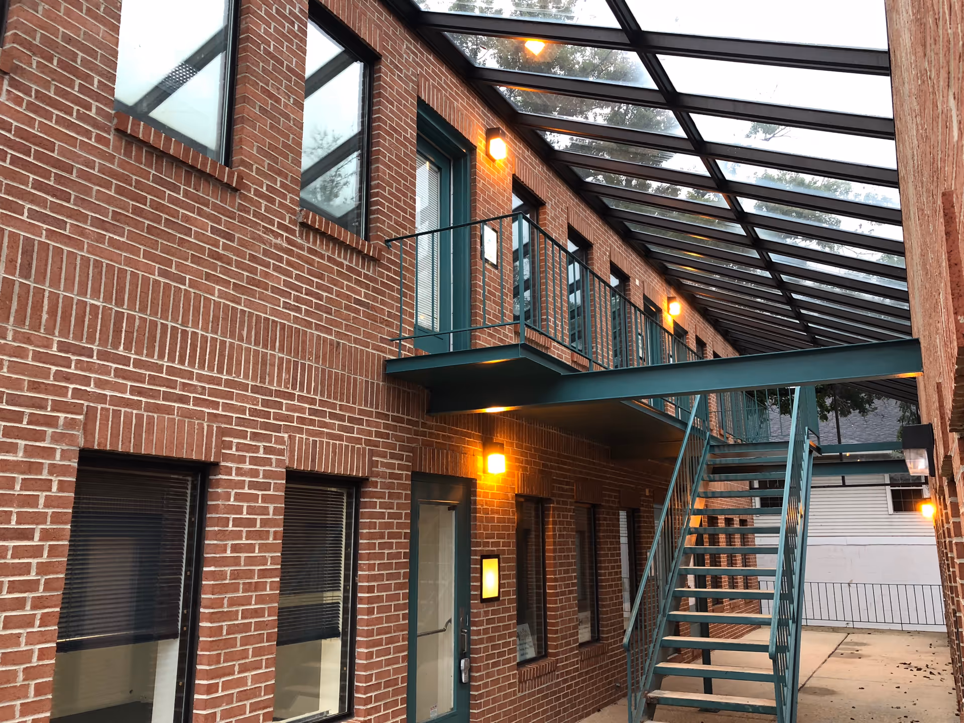 Brick building exterior with a glass-covered walkway, metal stairs, and balconies.