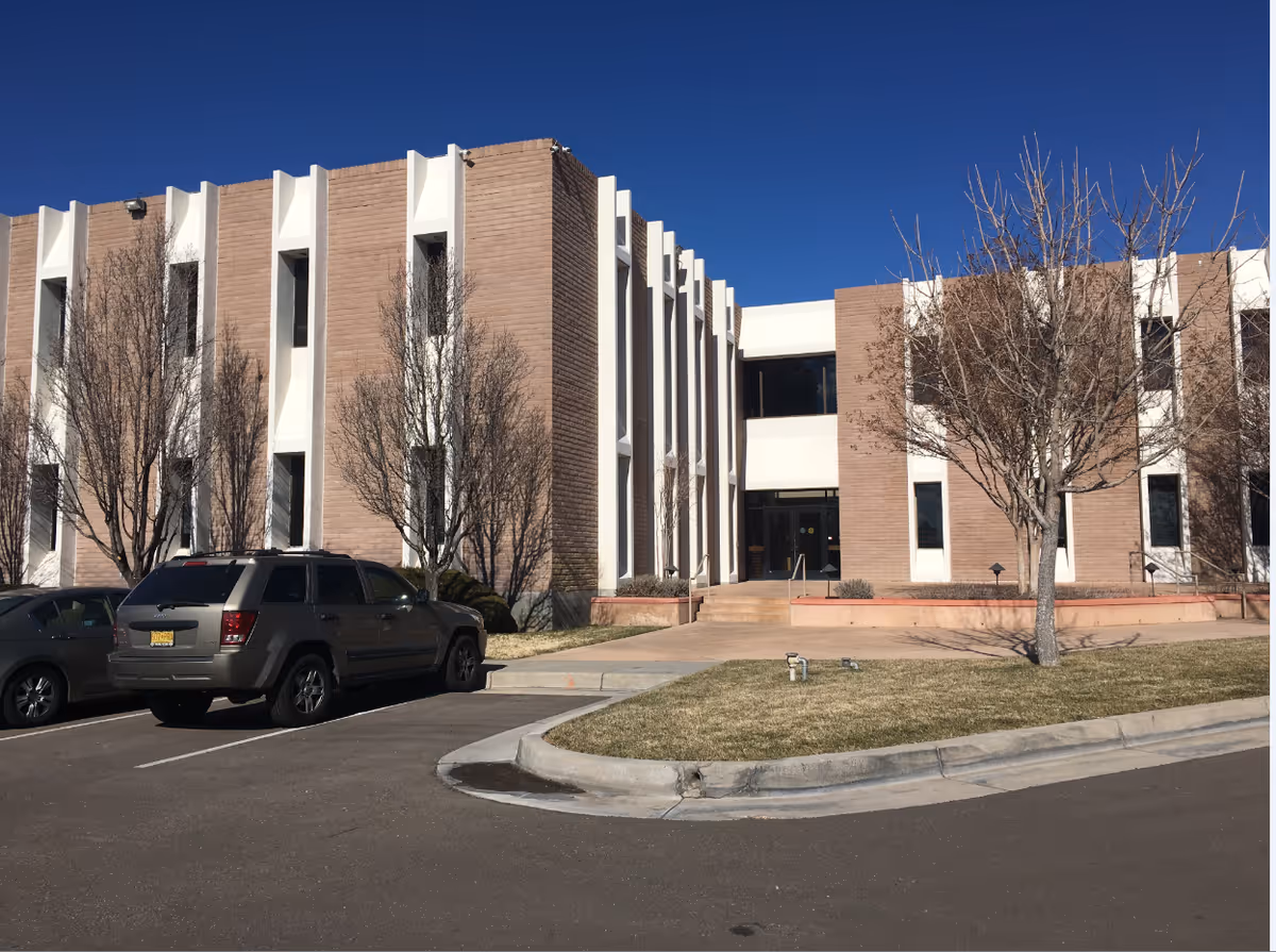 Exterior view of BAYADA Assistive Care building with brick and white façade, parking lot, and trees.