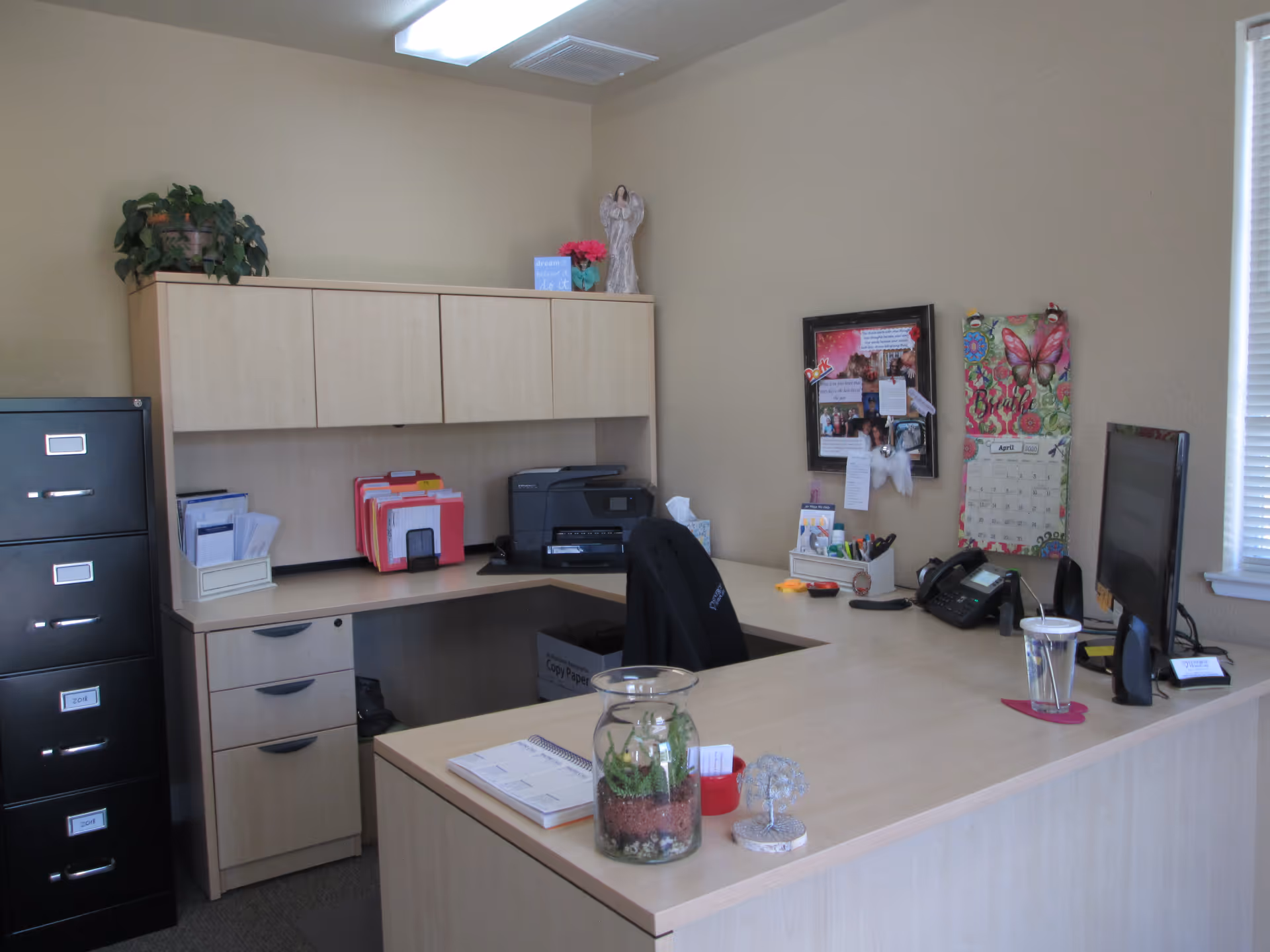 An office reception area in a senior care facility with a large desk, computer, and cabinets.