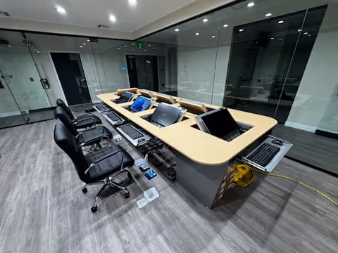 A modern conference desk with laptops and chairs inside a glass-walled meeting room.
