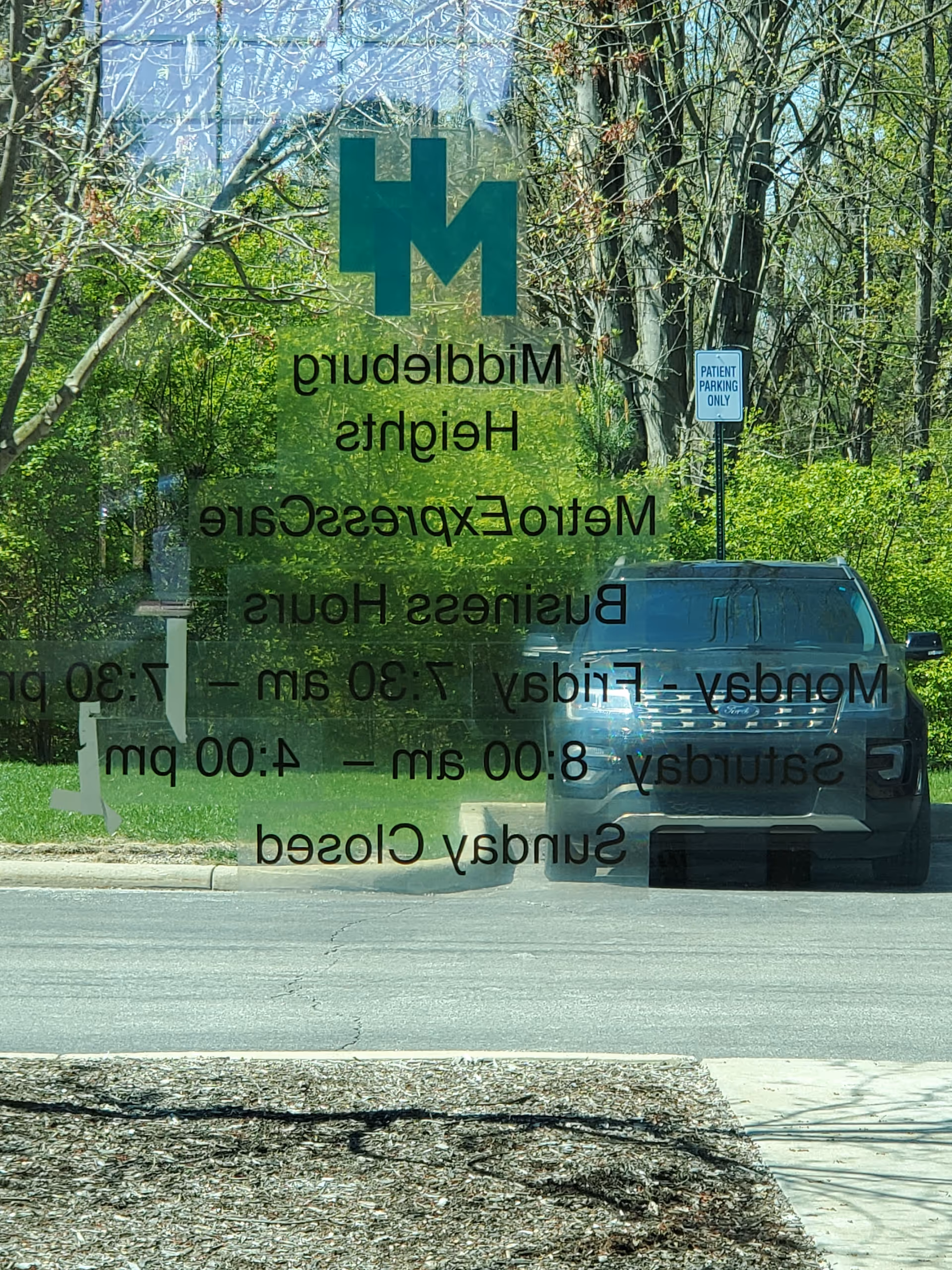 Glass reflection shows MetroHealth Middleburg Heights signage with a parked SUV and trees.
