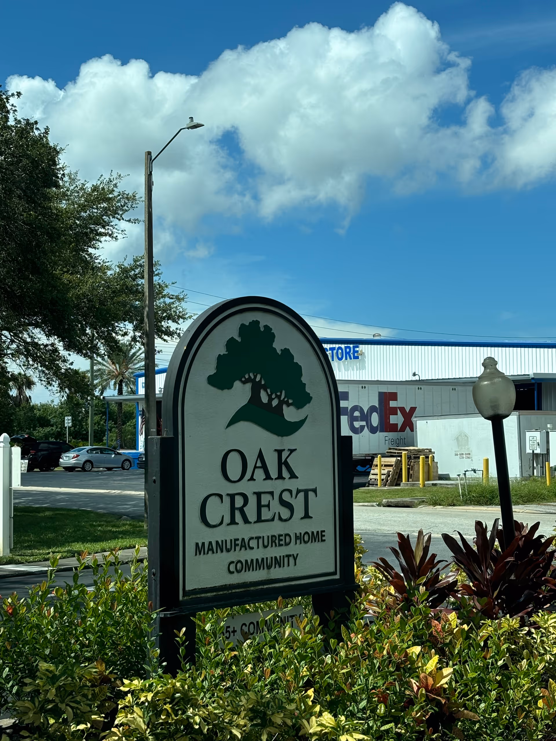 Outdoor view of Oak Crest Manufactured Home Community sign with a FedEx building in the background.