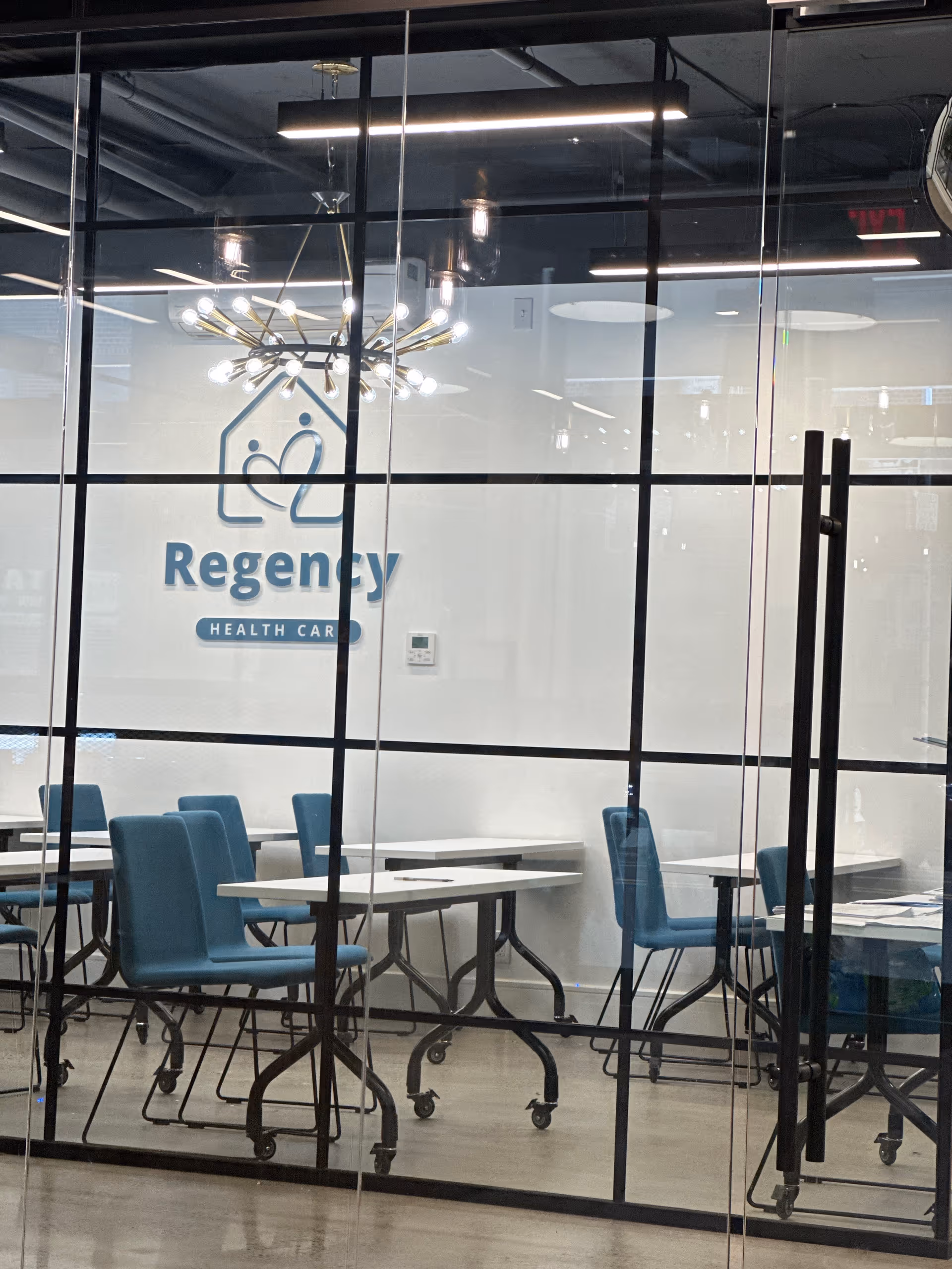 Glass-walled dining area with blue chairs and white tables in Regency Health Care facility.