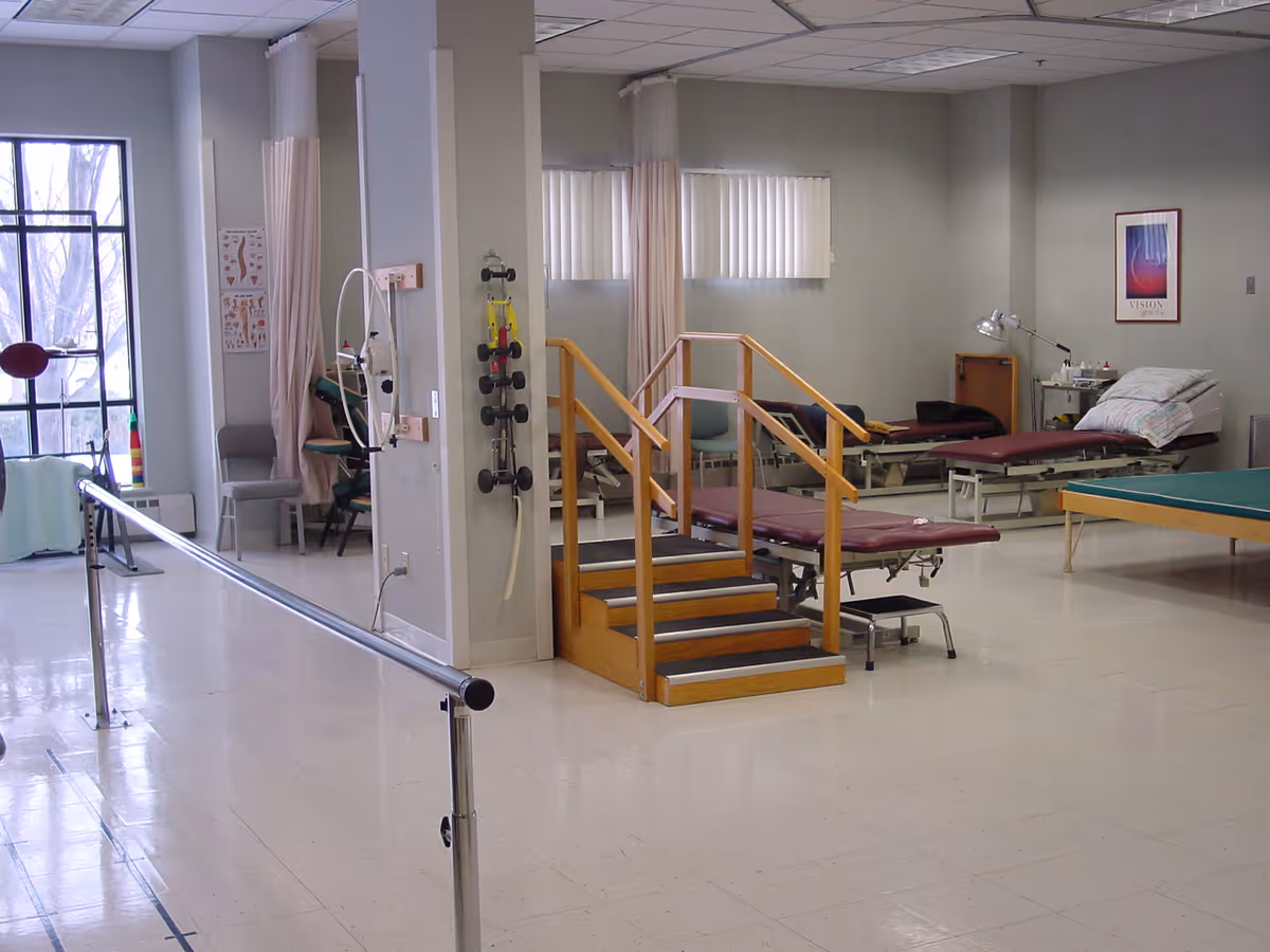 Interior rehabilitation gym room with therapy equipment, parallel bars, steps, and treatment beds.