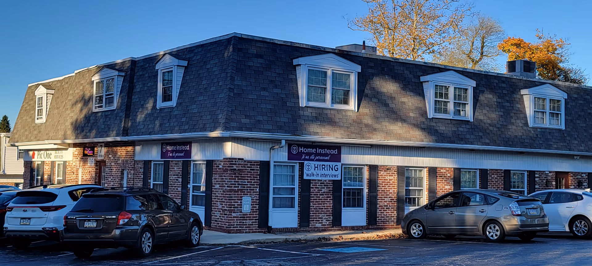A brick facility with Home Instead signage and several parked cars along the front.