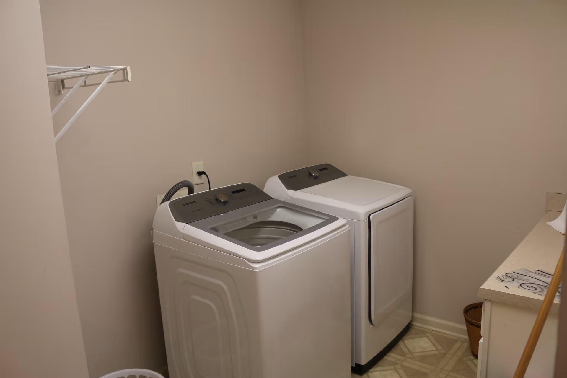A compact laundry room with a washer, dryer, shelves, and a countertop.