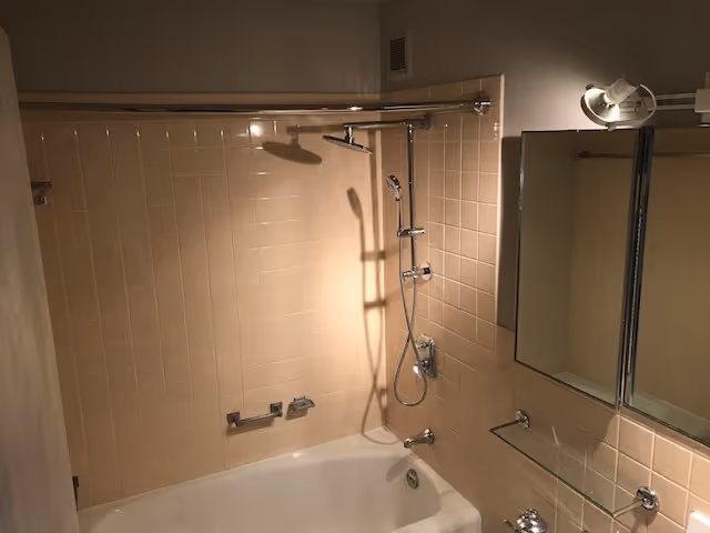 Beige tiled bathroom with a bathtub, handheld shower, and wall-mounted mirror.