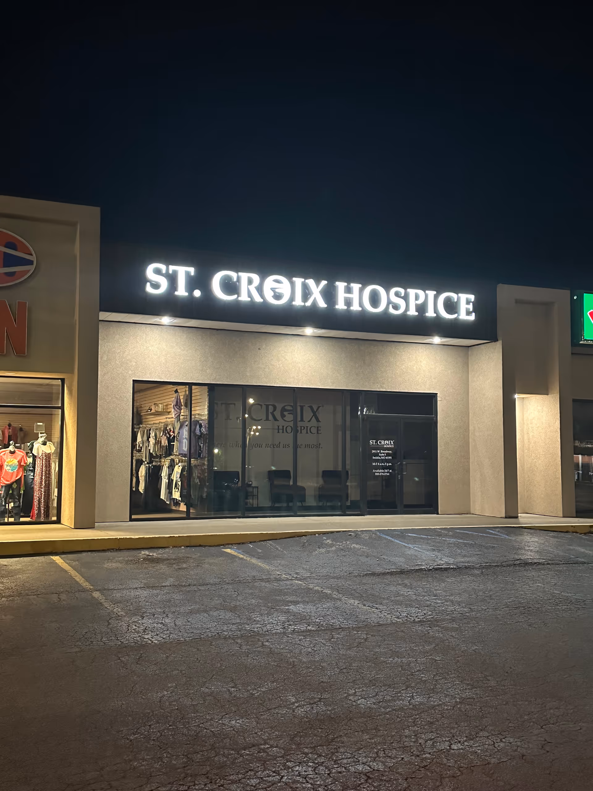 Night exterior of a storefront with illuminated ST. CROIX HOSPICE sign and glass entry.