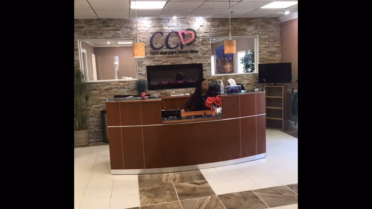 Reception desk in a lobby with stone wall, logo, plants, and a staff member.