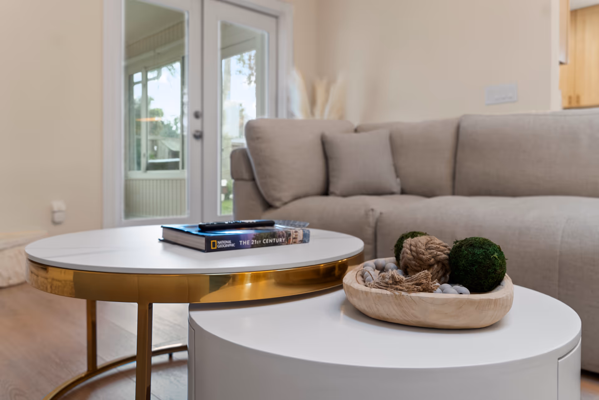 Modern living room with beige sofa, white coffee tables, and decorative centerpiece.