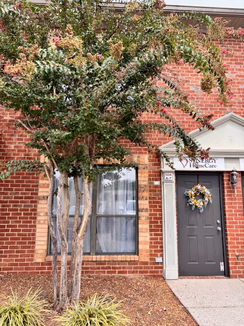 Brick exterior with a front entrance, tree, wreath, and Synergy HomeCare sign.