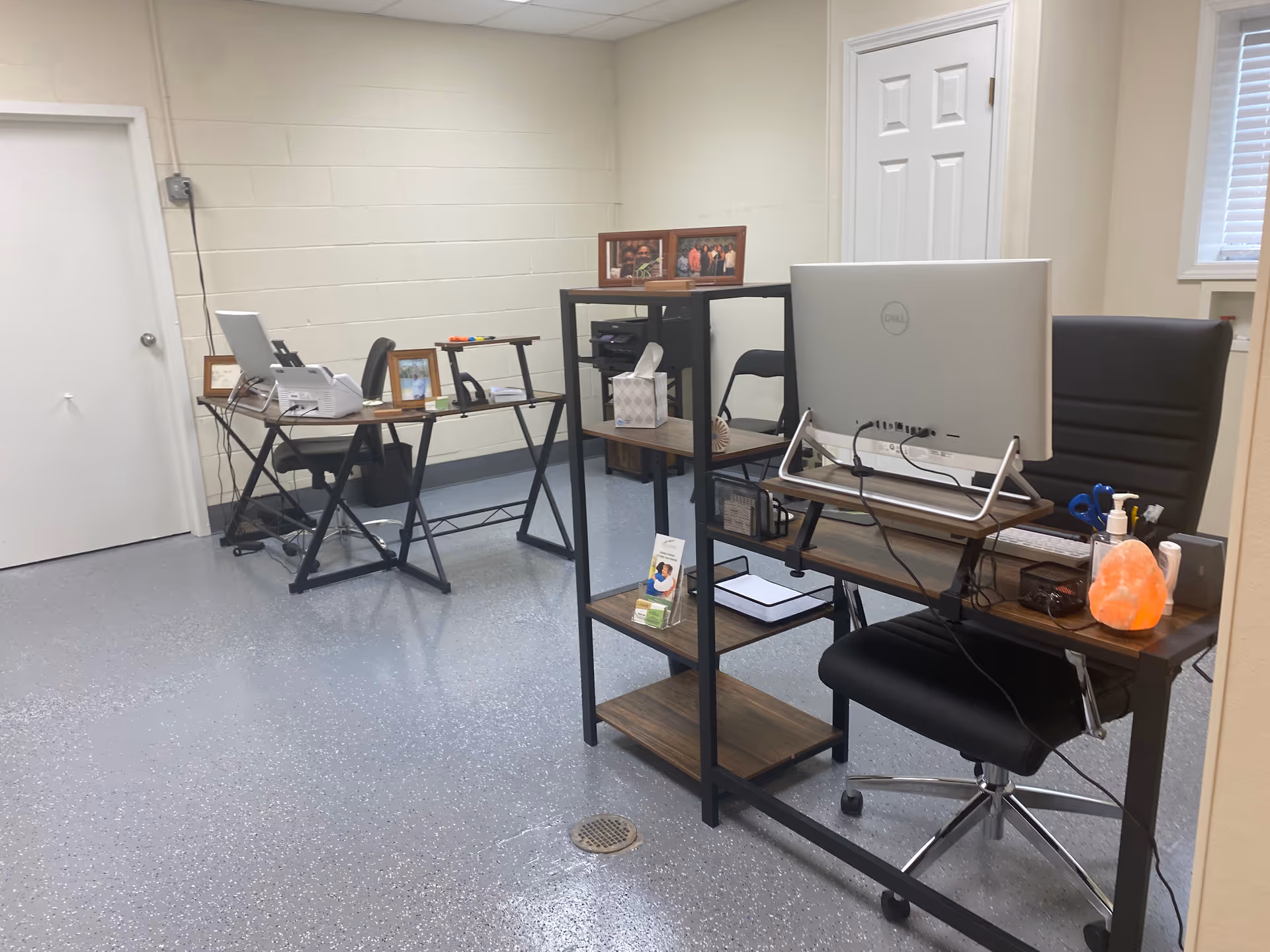 Office area with desks, computers, shelves, and framed photos in a clean, organized room.