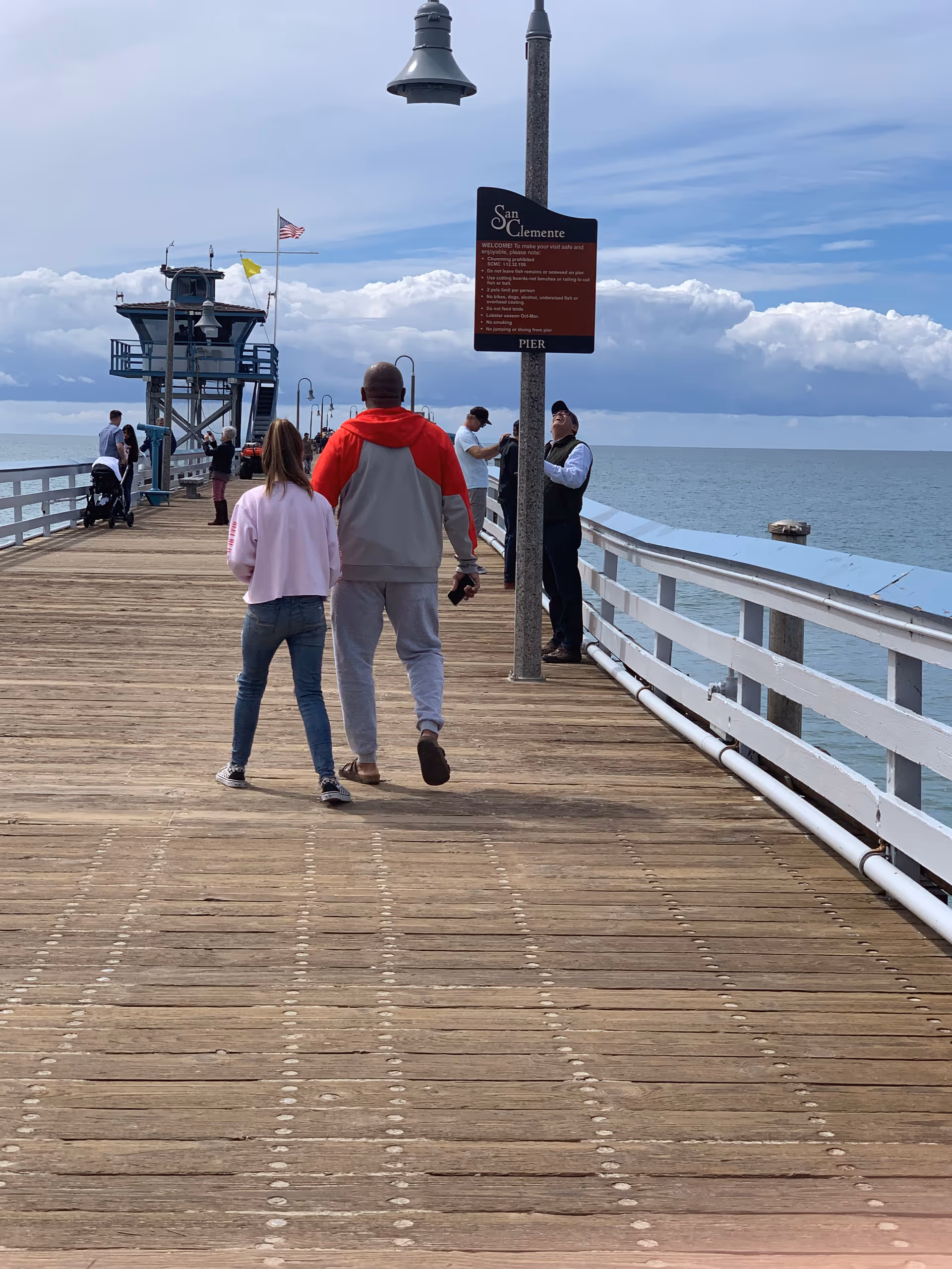 Wooden pier extends over the ocean with people walking and a signboard.