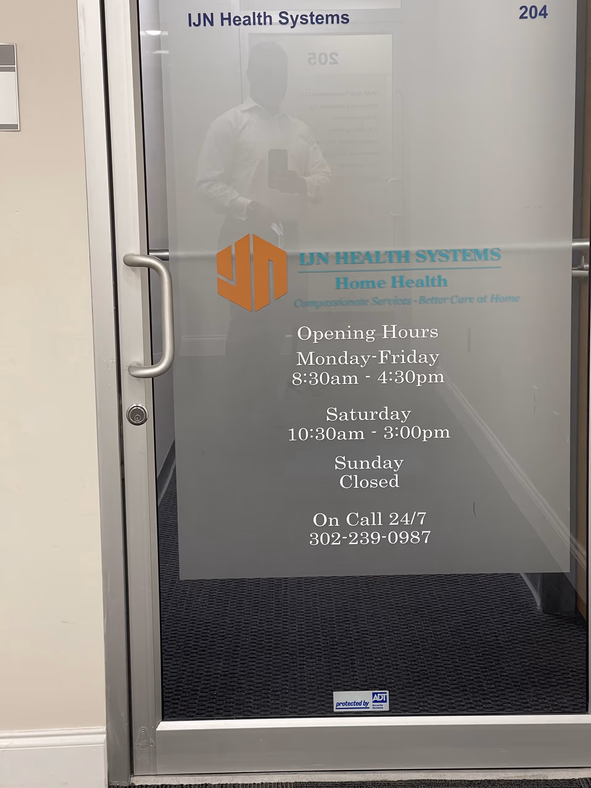 Glass door with IJN Health Systems logo and hours; reflection of a person.