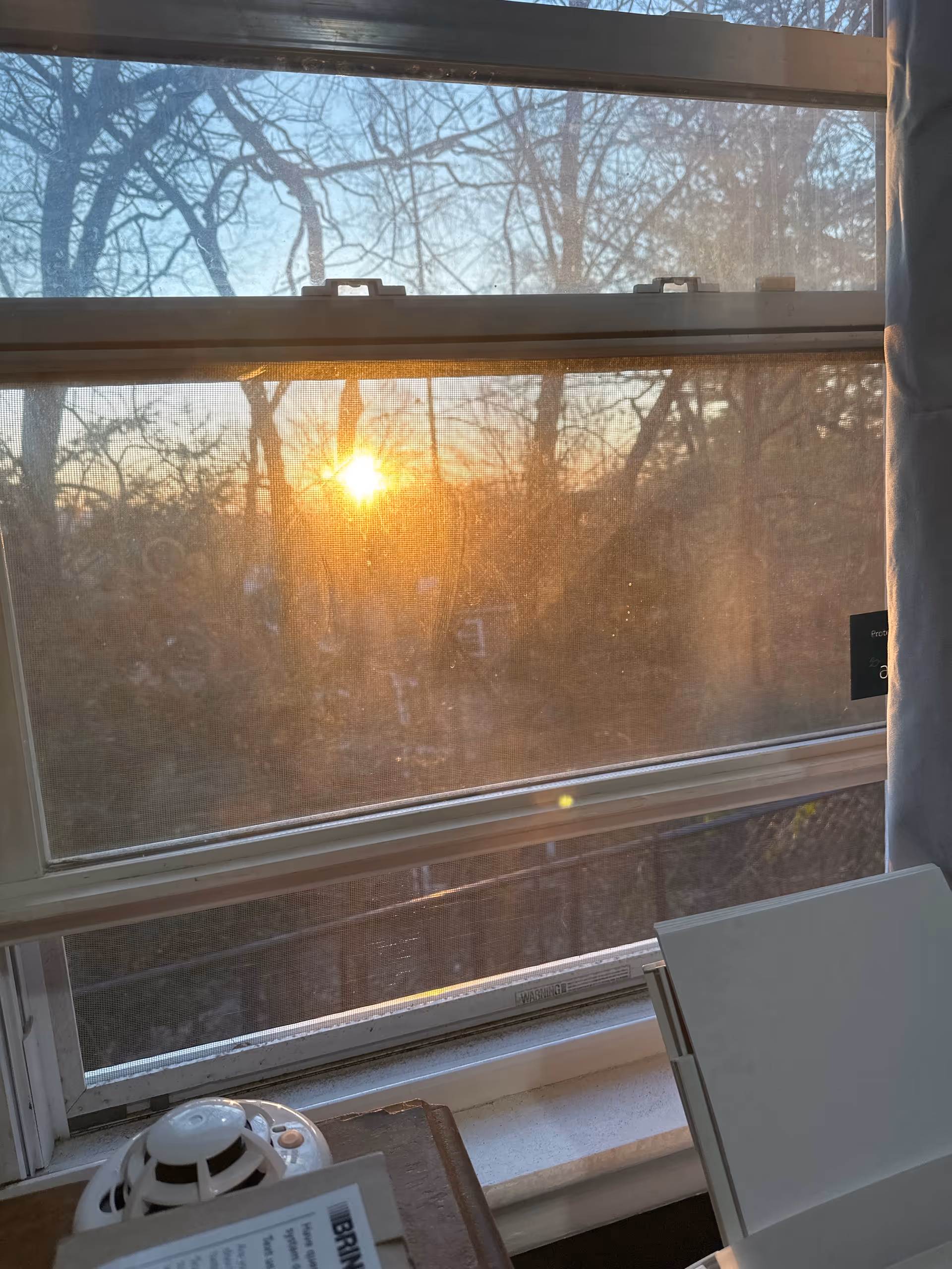 Sunset seen through a large window, indoors with a desk, papers, and a small fan.