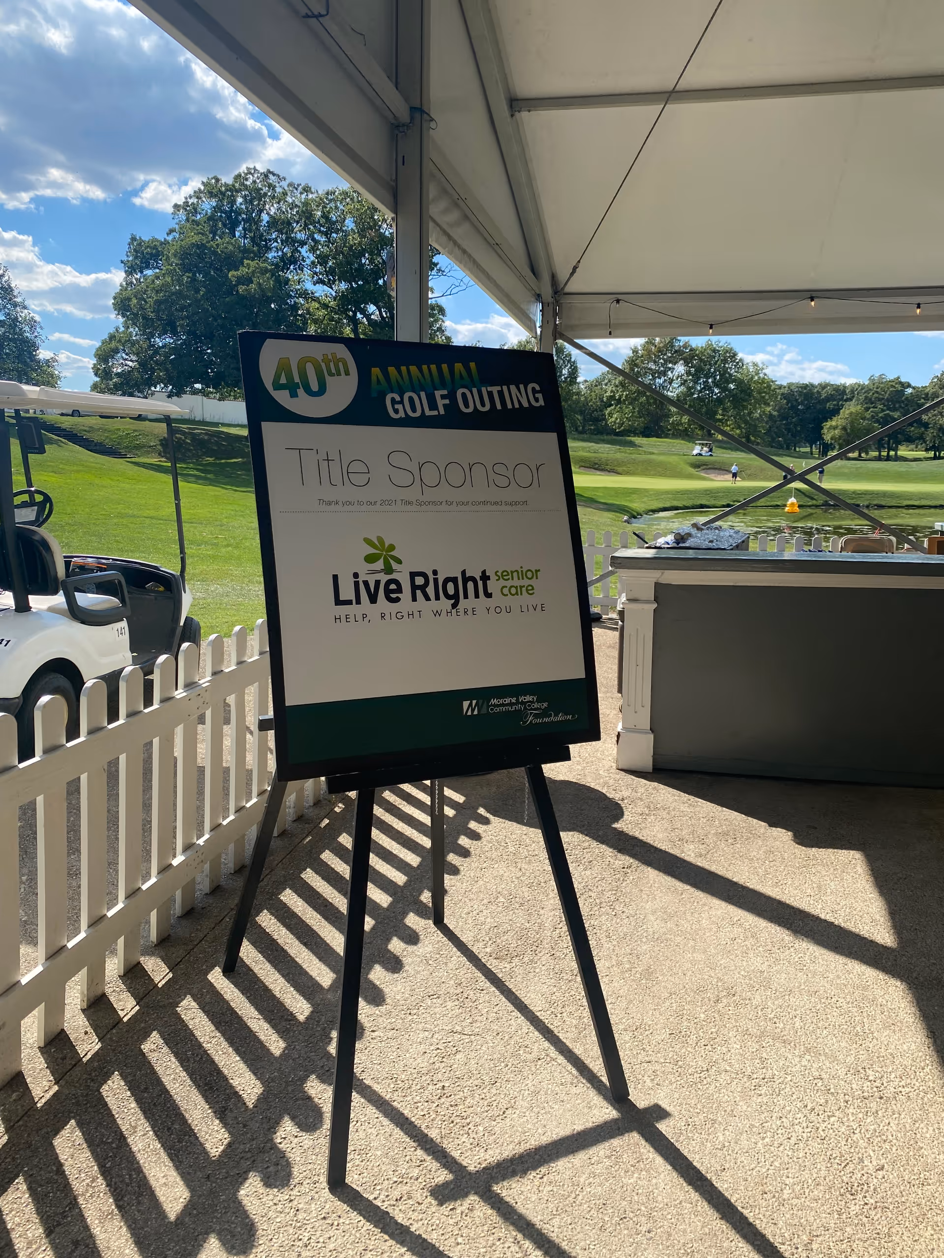 Outdoor event sign for a golf outing sponsored by Live Right Senior Care under a tent.