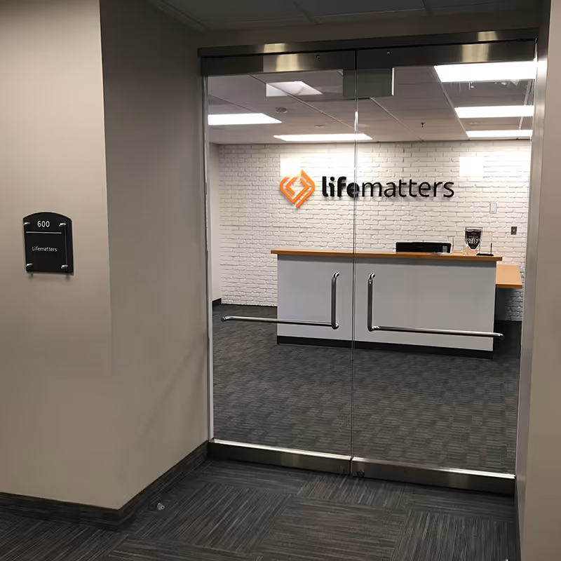 Glass doors open to a reception desk with a Lifematters logo on a brick wall.