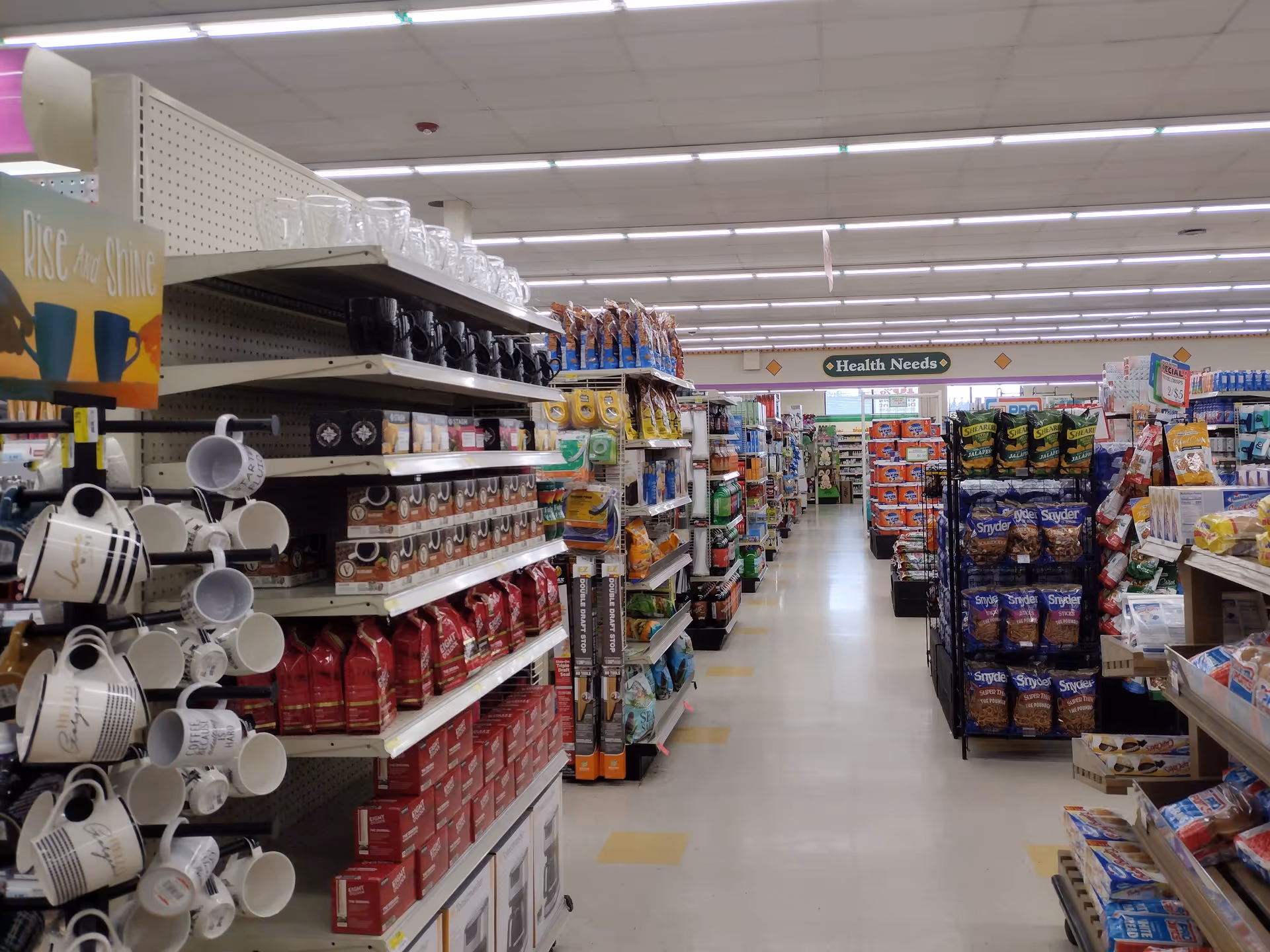 Bright supermarket aisle with shelves of mugs, coffee, and snacks in Discount Drug Mart.