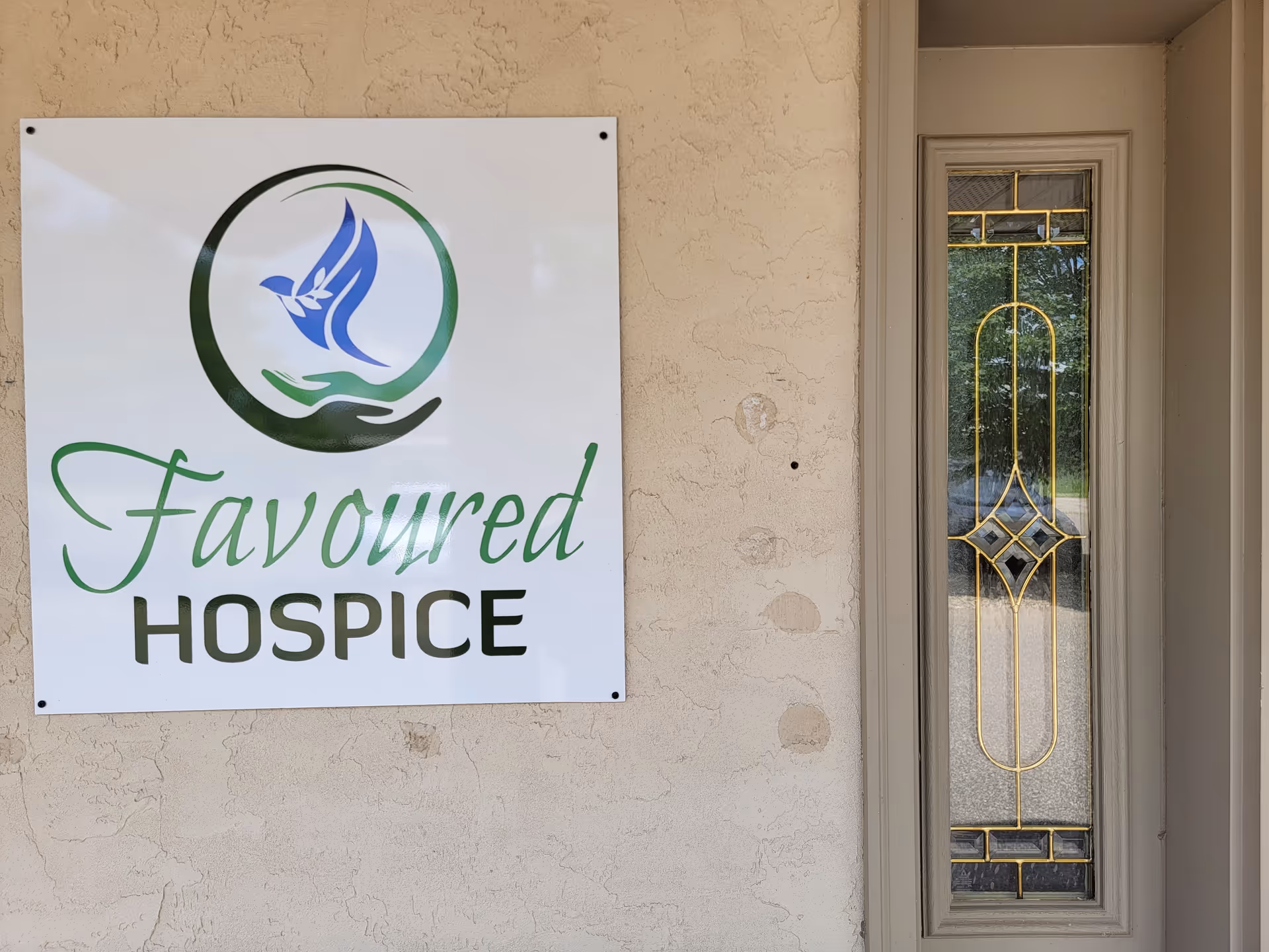 Exterior wall with a 'Favoured Hospice' sign and a decorative glass entrance door.