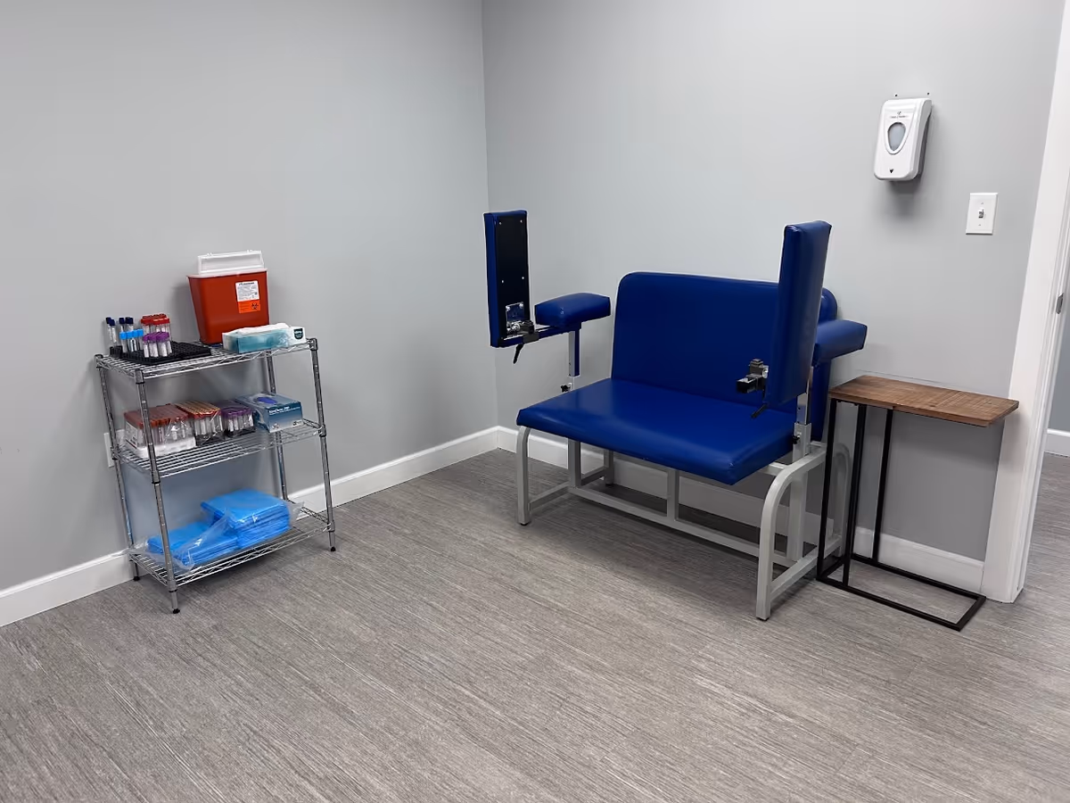 Blue padded medical chair in a small examination room with a supply cart.
