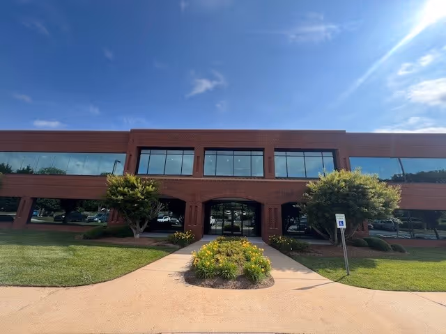 A brick two-story building with large windows and a landscaped entrance path.