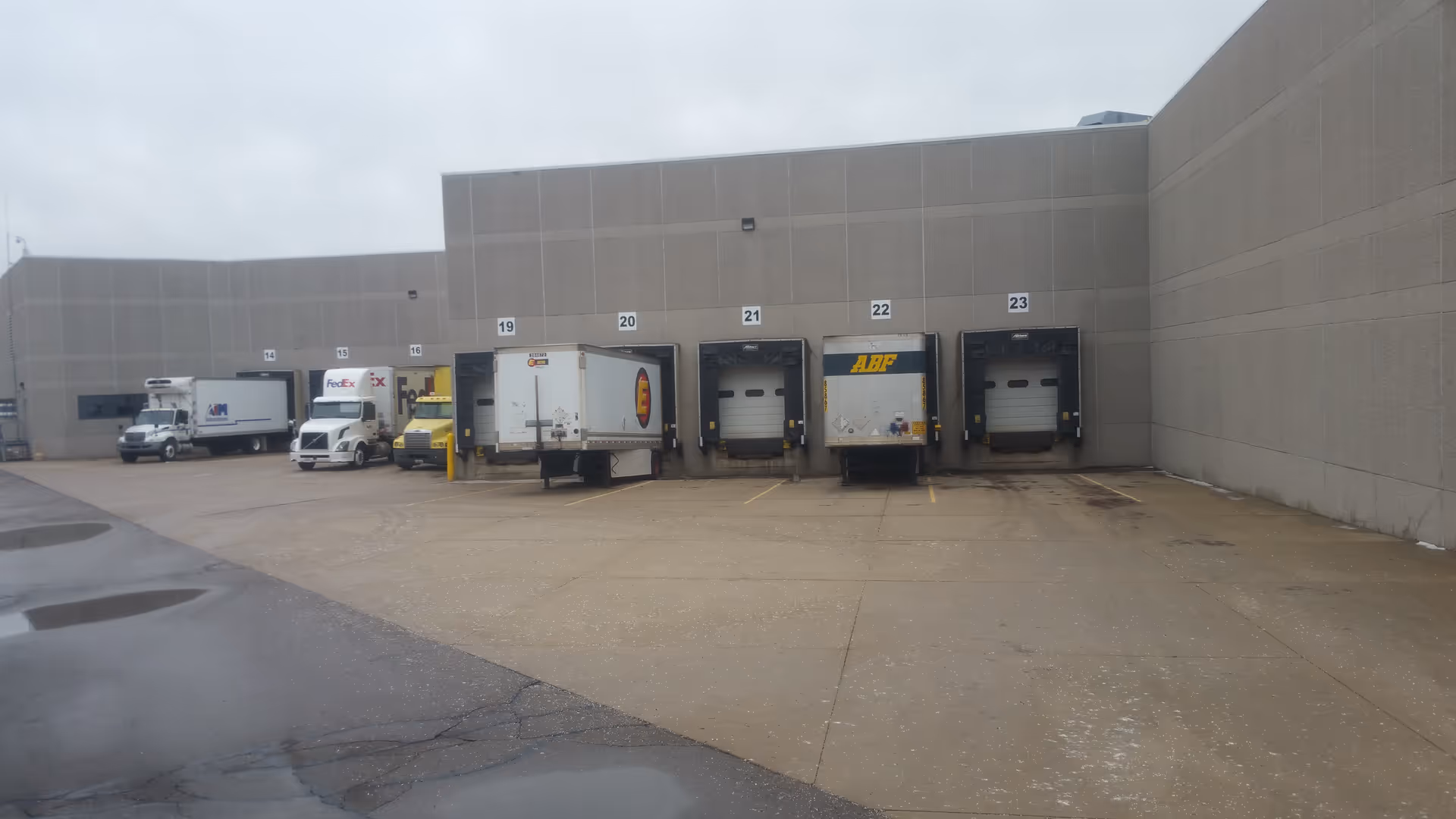 Exterior loading dock area with multiple bays and delivery trucks beside a gray building.
