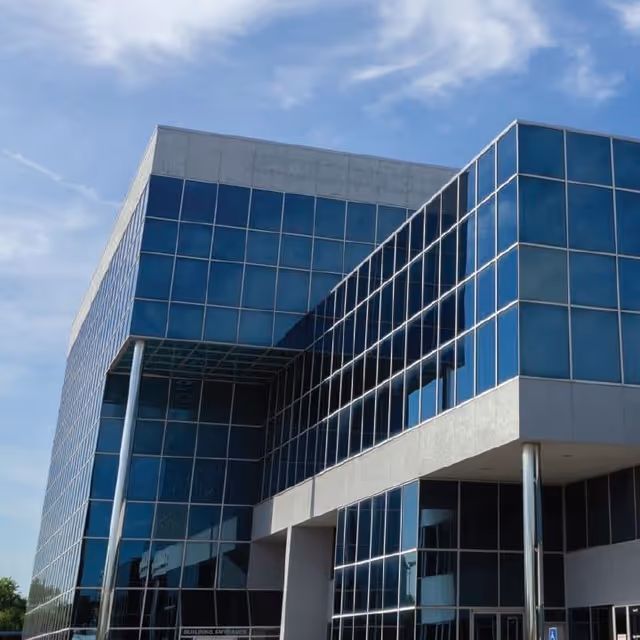 Modern glass-fronted building exterior with blue-tinted windows and concrete accents.