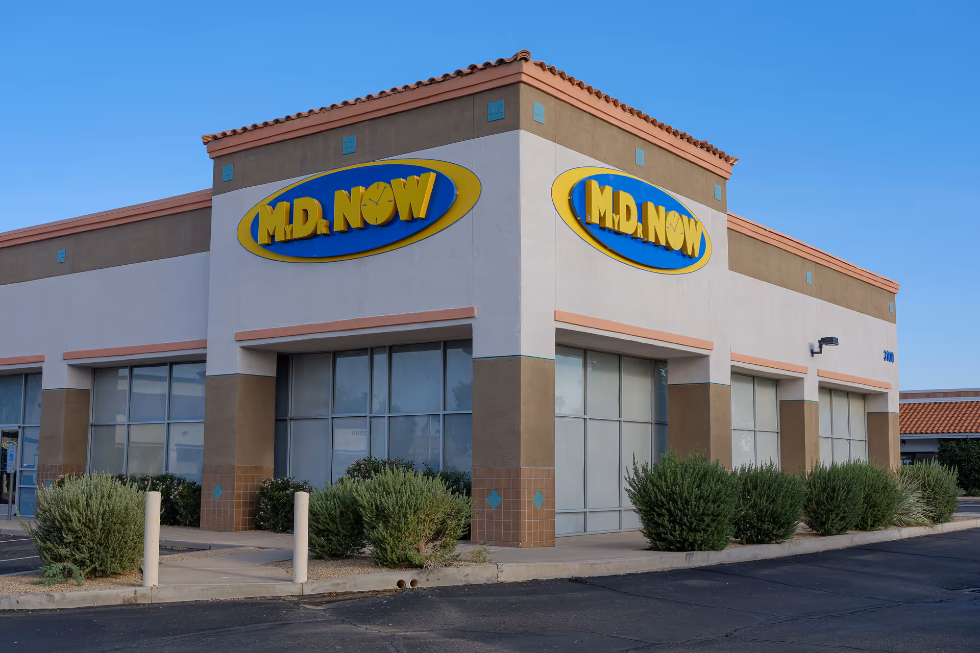 Exterior view of a beige building with large MD NOW sign and shrubs in front.