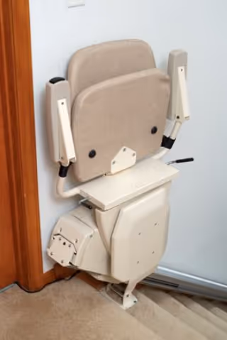 A beige stairlift chair mounted on a staircase beside a wall.