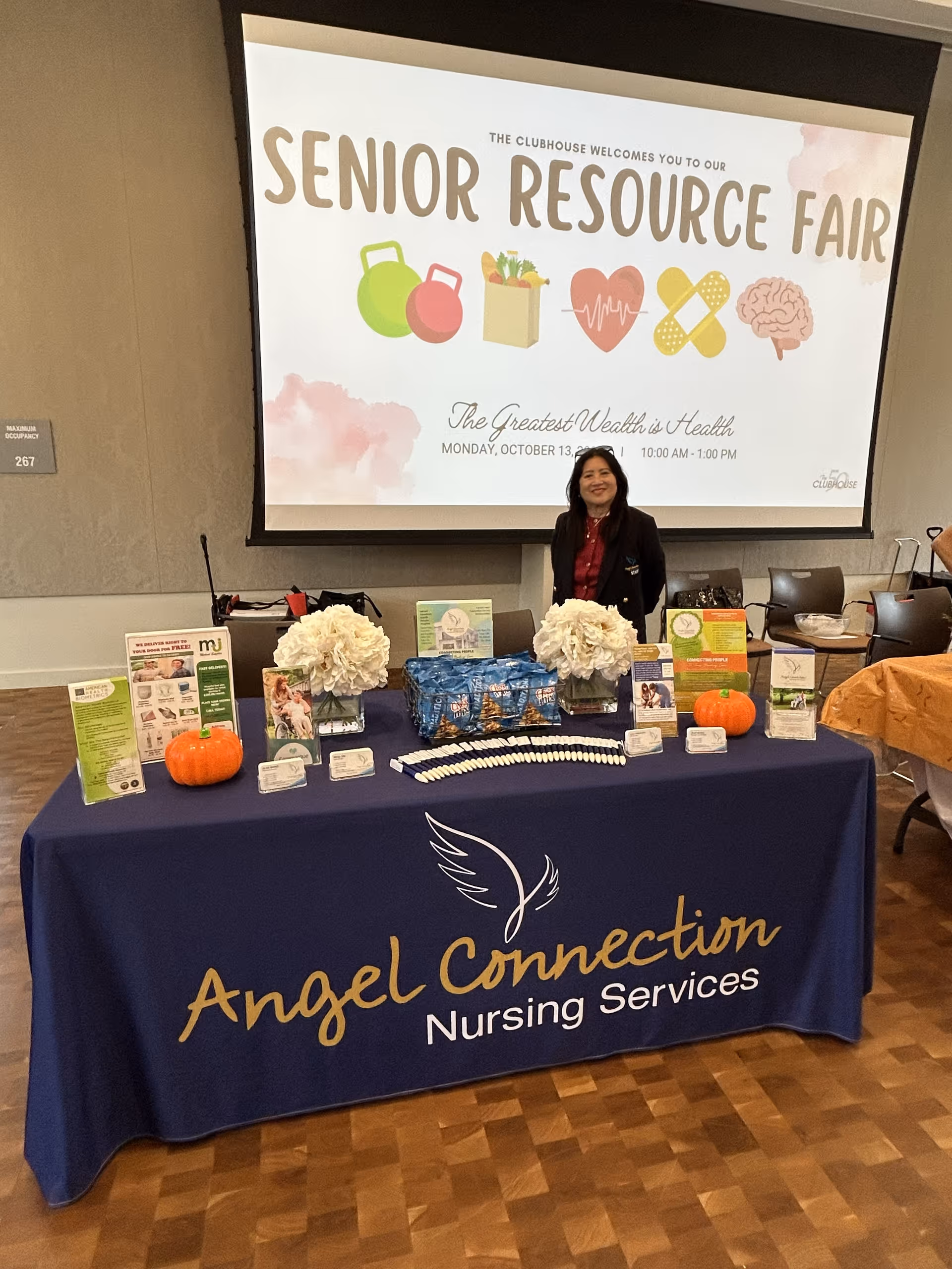 Table with Angel Connection Nursing Services banner at a senior resource fair in a conference hall.