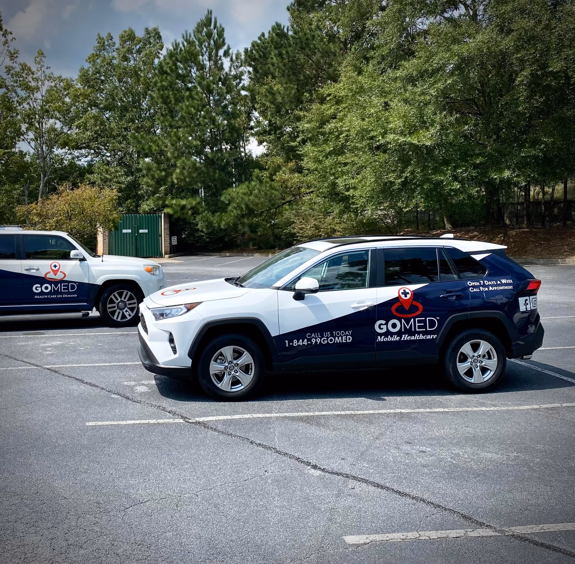 Two branded GOMED Mobile Urgent Care vehicles parked in a tree-lined lot.