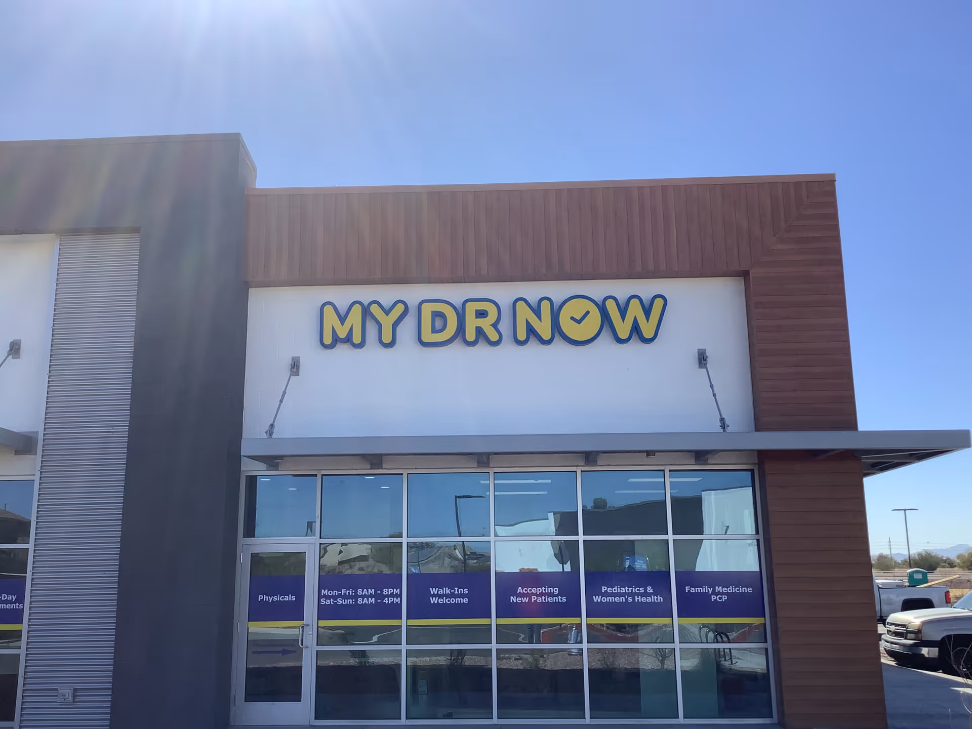 Exterior view of MY DR NOW building with large sign and glass storefront under blue sky.