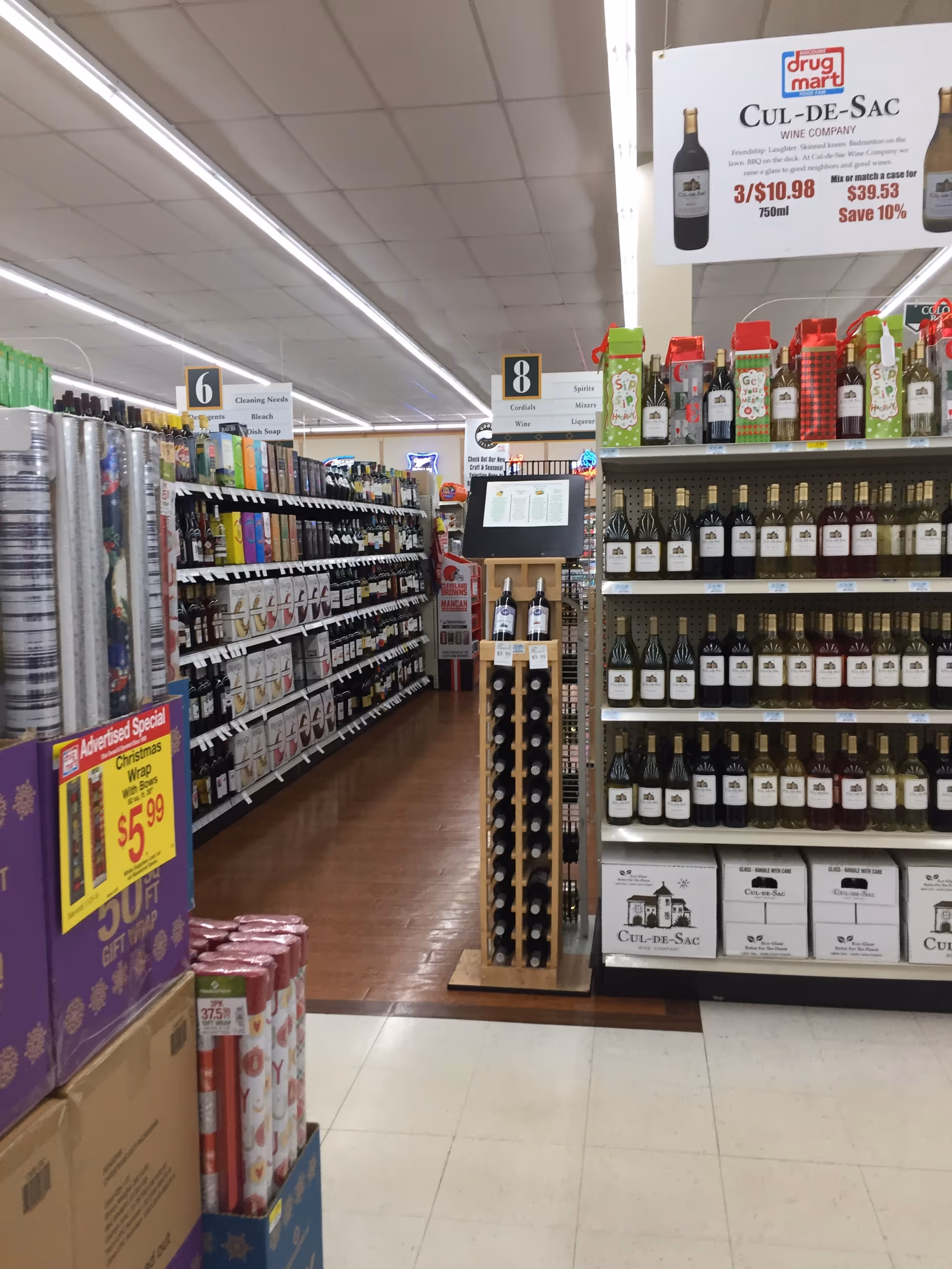 Inside a Discount Drug Mart aisle with wine bottles and promotional signage.