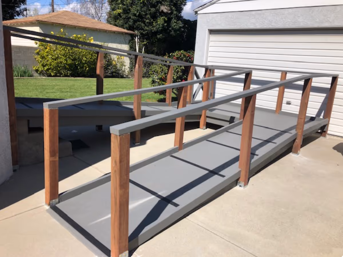 Exterior concrete ramp with wooden railings leading to a white garage door.