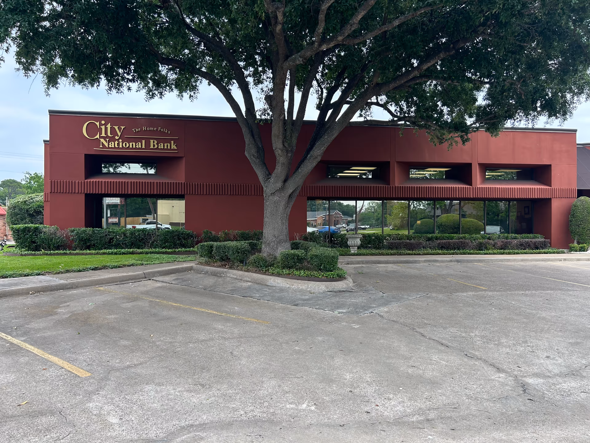 Red City National Bank building with a large tree in front and an empty parking lot.