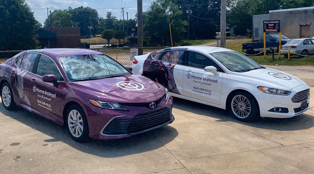 Two branded Home Instead cars parked in a lot beside a chain link fence.