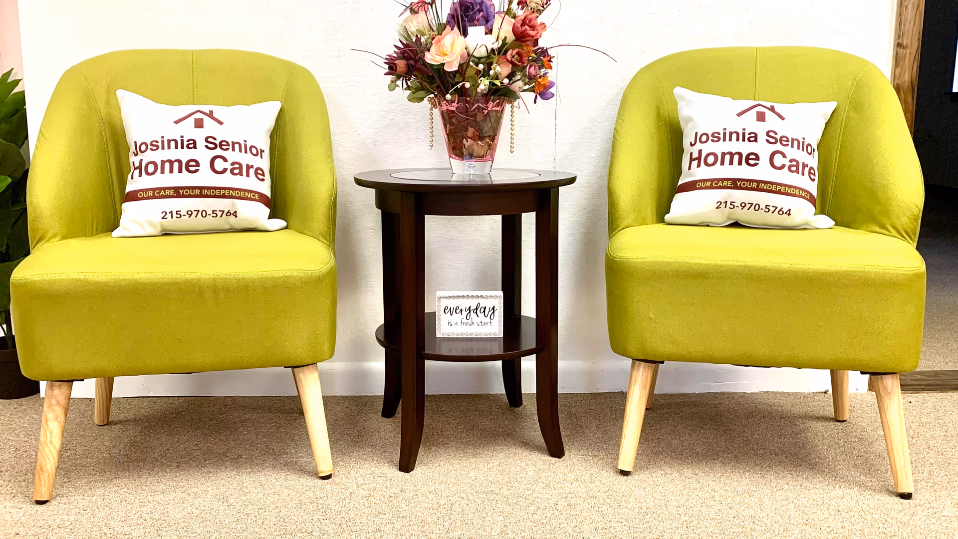 Two lime-green armchairs flank a round table with a flower arrangement in a waiting area.