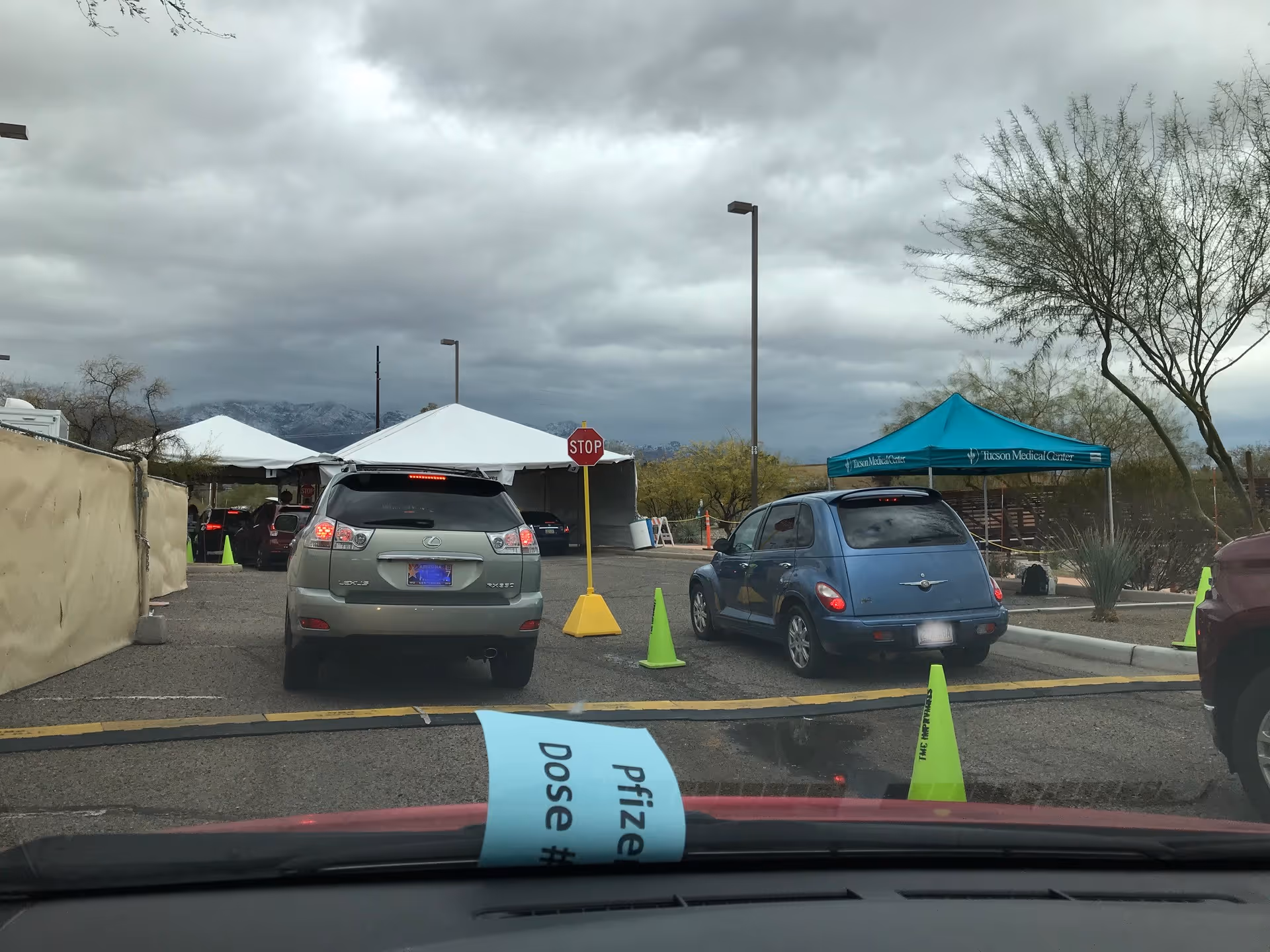Parking lot exterior with white tents, traffic cones, and a stop sign under cloudy skies.