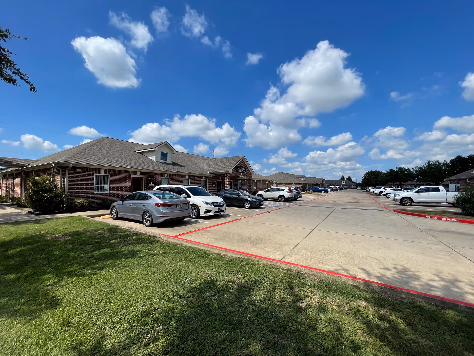 Exterior view of a brick senior living facility with a parking lot and blue sky.