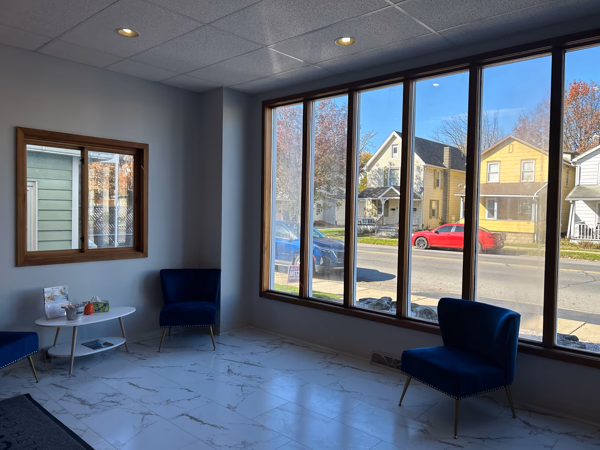 Bright interior lobby with large windows, blue chairs, and a round coffee table.