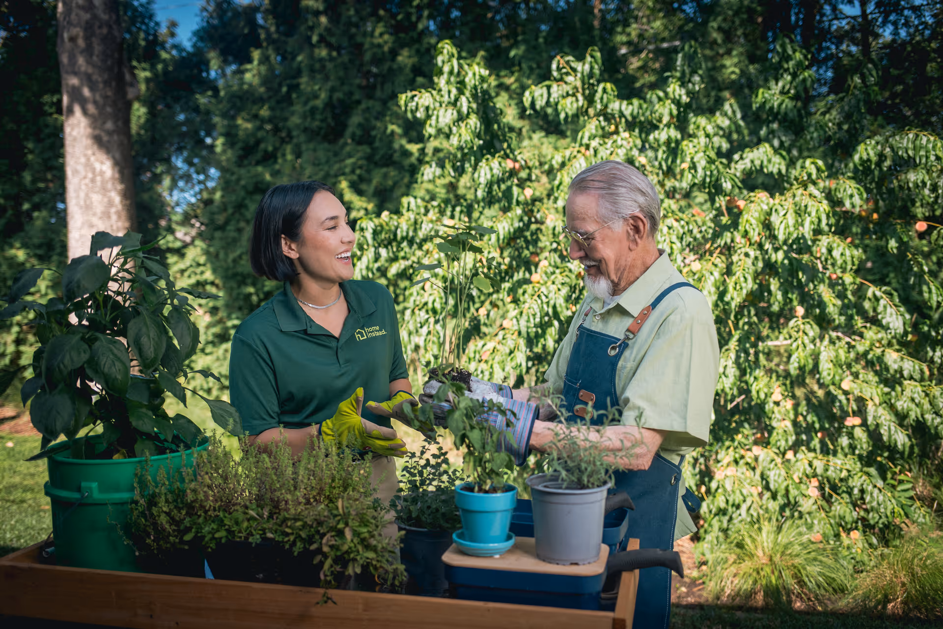 Caregiver and senior gardening outdoors, smiling near potted plants on a wooden table