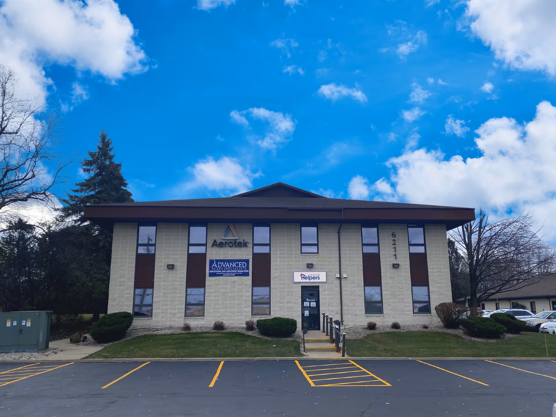 Two-story beige building with Senior Helpers sign, entrance stairs, parking lot in front.