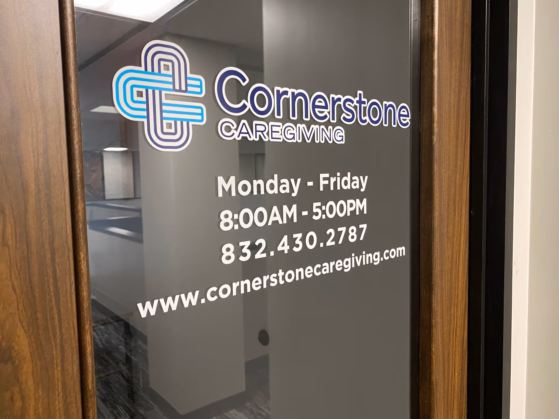 Glass door of Cornerstone Caregiving displays logo, hours, phone number, and website.