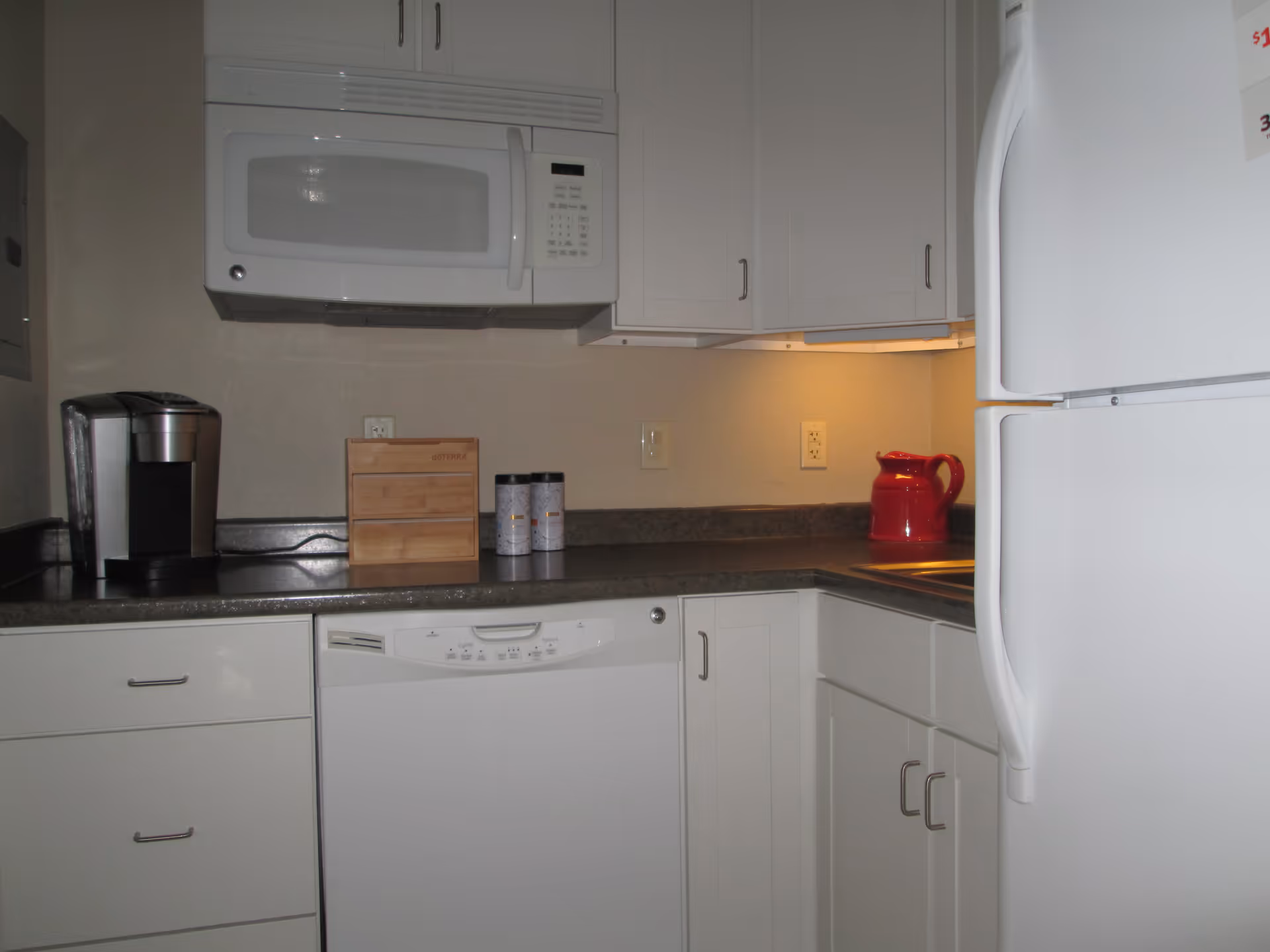 White kitchen with microwave, dishwasher, refrigerator, and red kettle on the counter.