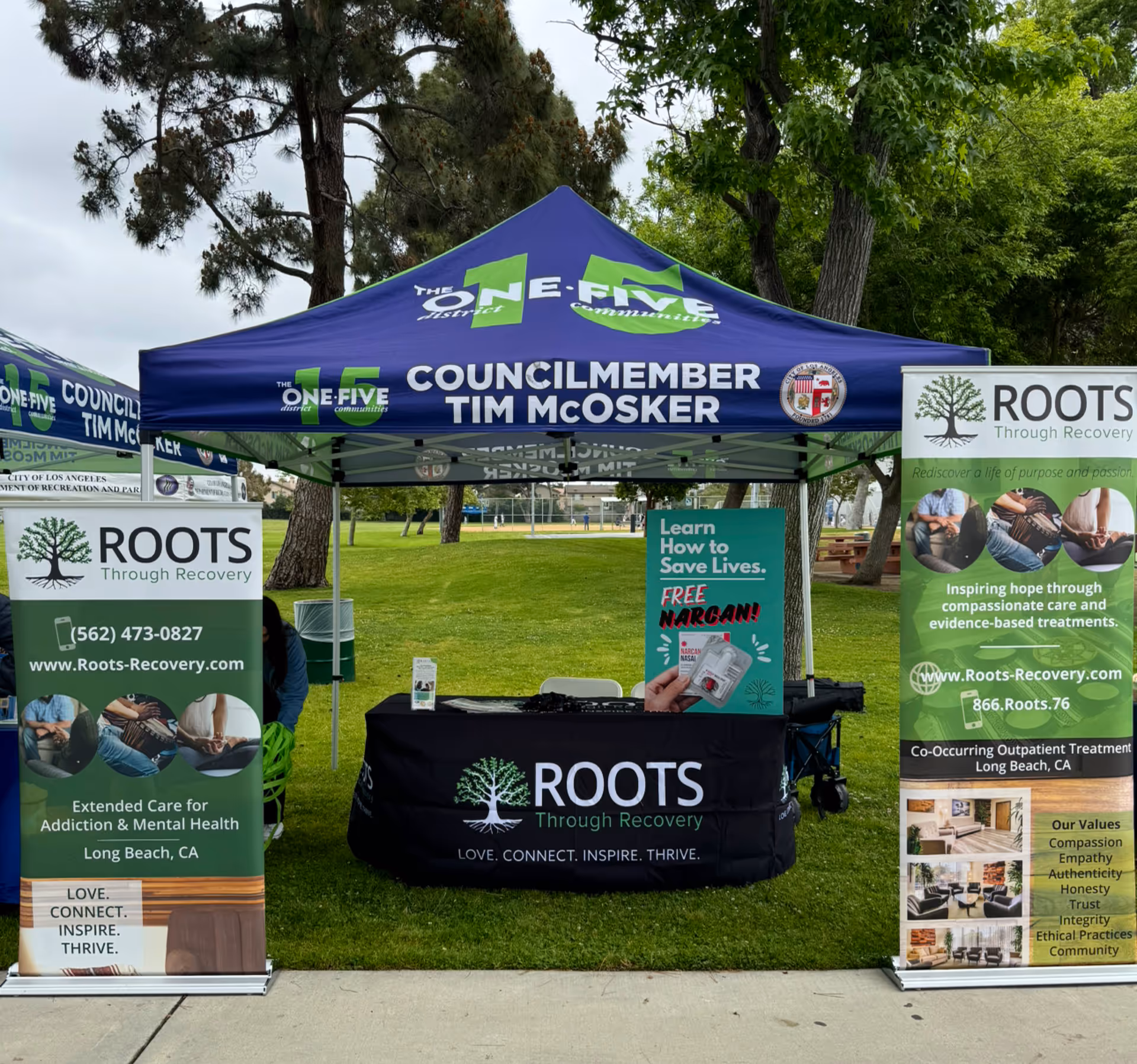 Outdoor information booth with Roots Through Recovery banners at a park.