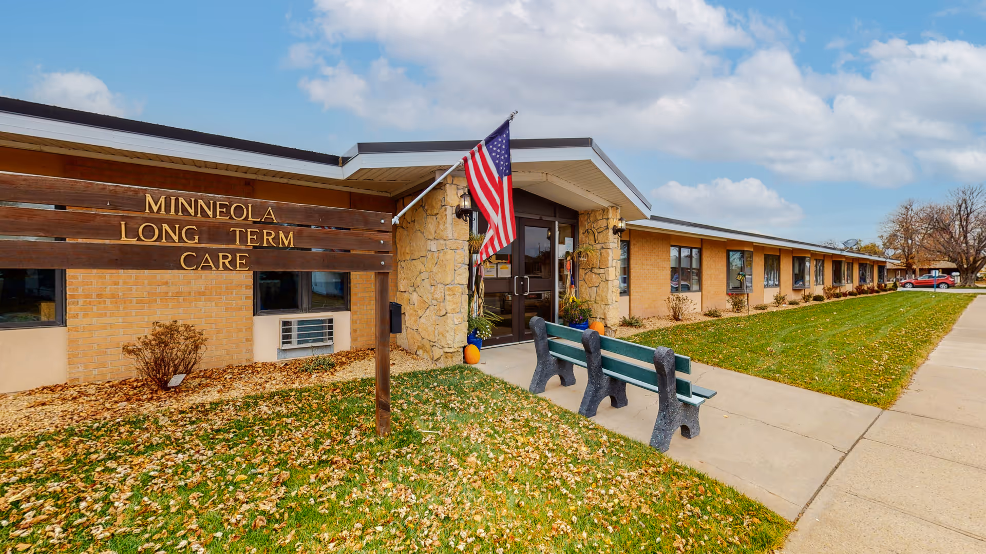 Exterior view of Minneola Long Term Care facility with entrance, flag, and benches.